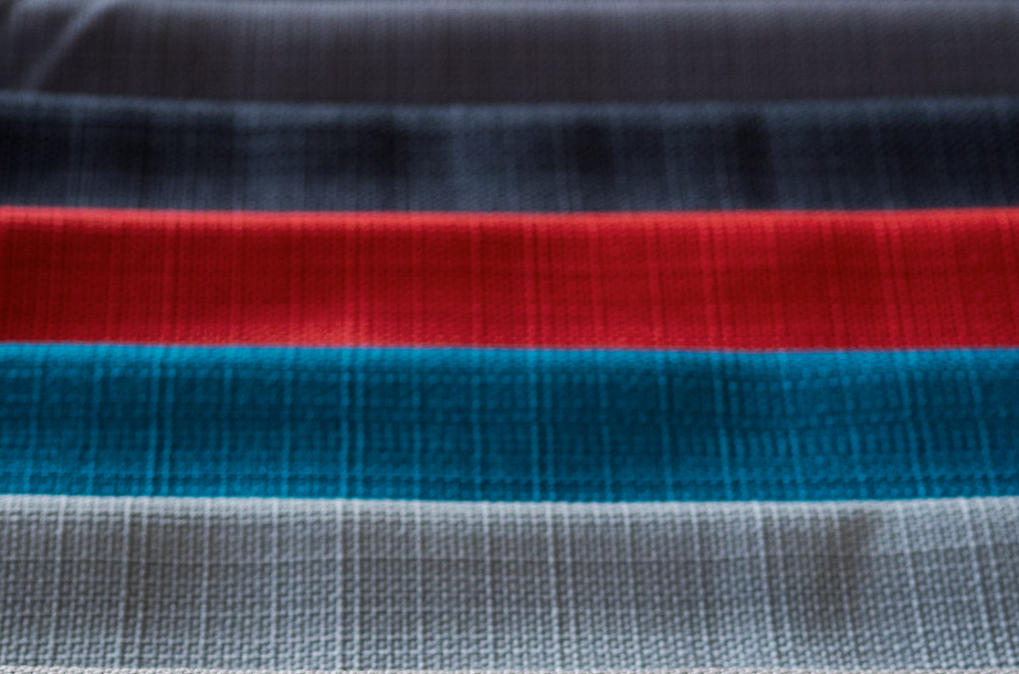 Close-up of a textured fabric with horizontal stripes in shades of black, gray, red, blue, and white. The focus is sharp, emphasizing the fabric's weave detail to build engagement.