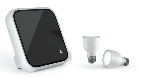 A black smart display with a curved edge next to two white LED smart bulbs, one standing upright and one lying sideways, all isolated on a white background, ideal for a smarter home.