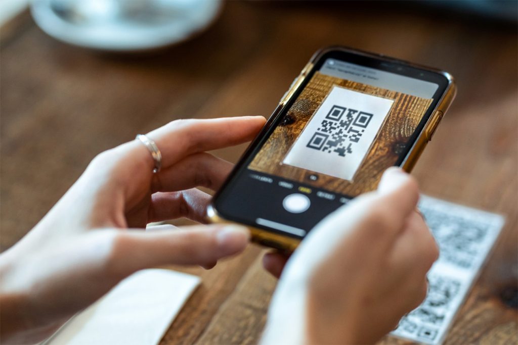 Hands holding a smartphone scanning a QR code on a wooden table, illustrative of consumer influence in digital interaction or technology use in daily transactions.