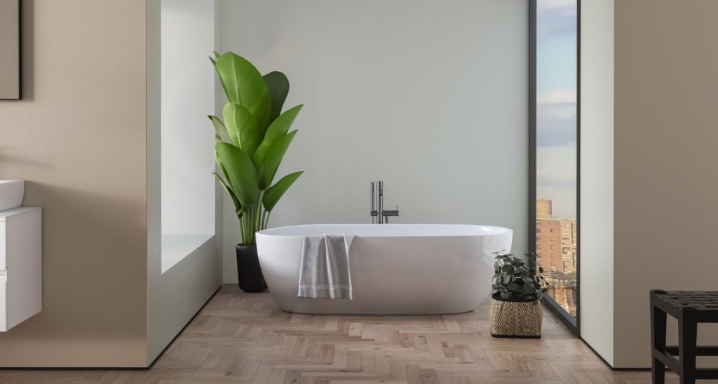 Modern bathroom with a freestanding white bathtub, wooden floor, a large green plant beside it, and floor-to-ceiling windows offering a city view enhanced by invisible design elements for aesthetic seamlessness.