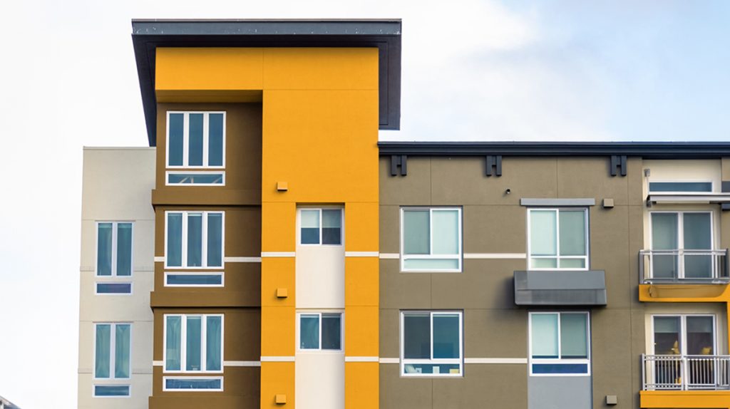 Modern apartment building facade with geometric patterns and a mix of yellow, orange, and gray colors under a clear blue sky, reflecting the latest trends in the building industry.