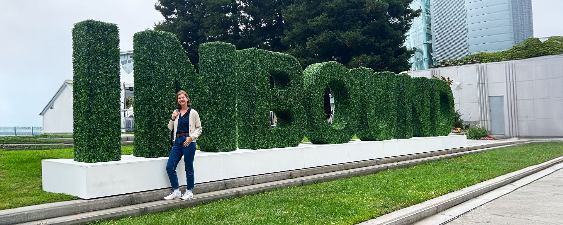A person stands smiling in front of large, green, hedge-like letters spelling "INBOUND" outdoors, with trees and modern buildings in the background—a perfect spot to discover new marketing tactics for B2B marketing and home building brands.