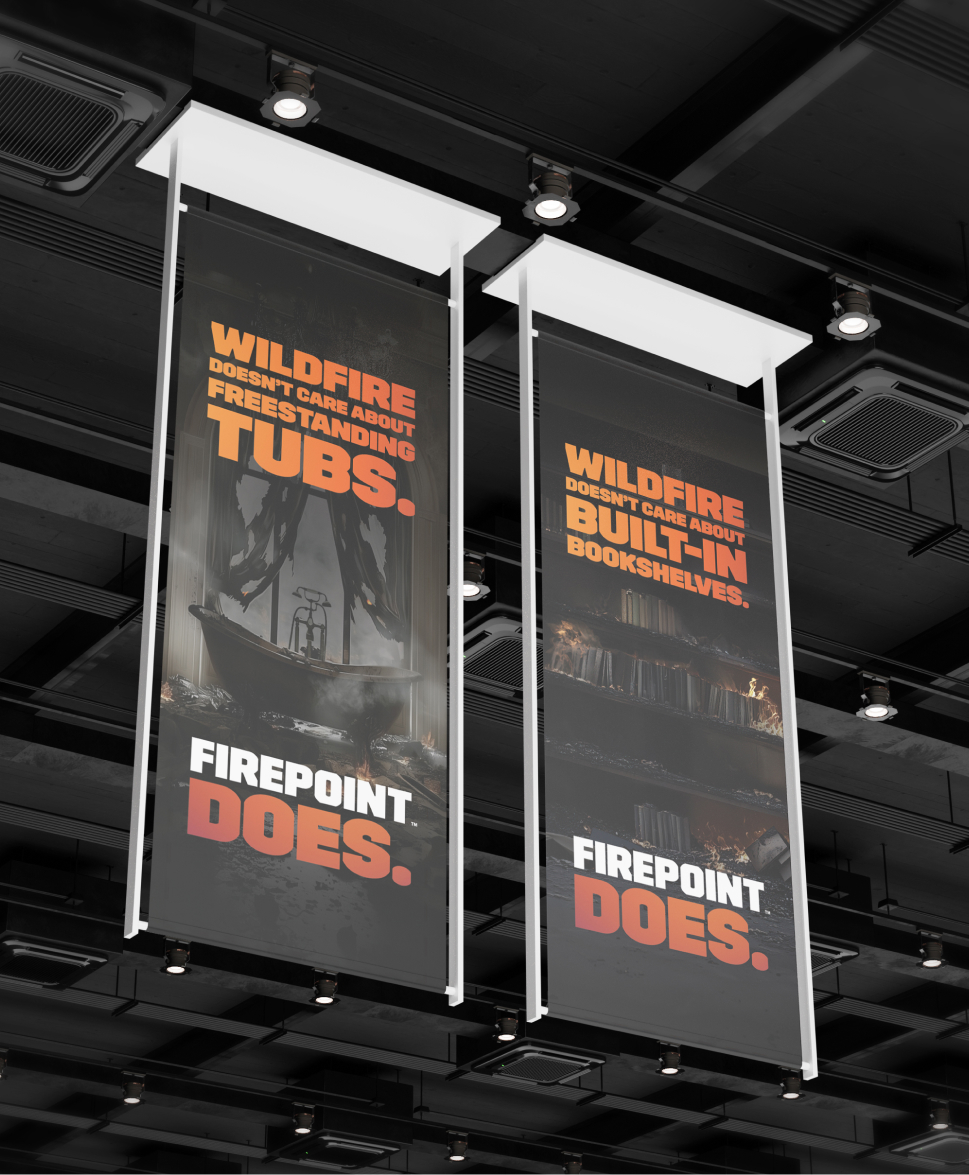 Two hanging banners in a modern building. The left banner reads, "Wildfire doesn't care about freestanding tubs. FIREPOINT DOES." with a bathtub image. The right banner reads, "Wildfire doesn't care about built-in bookshelves. FIREPOINT DOES." with bookshelves.
